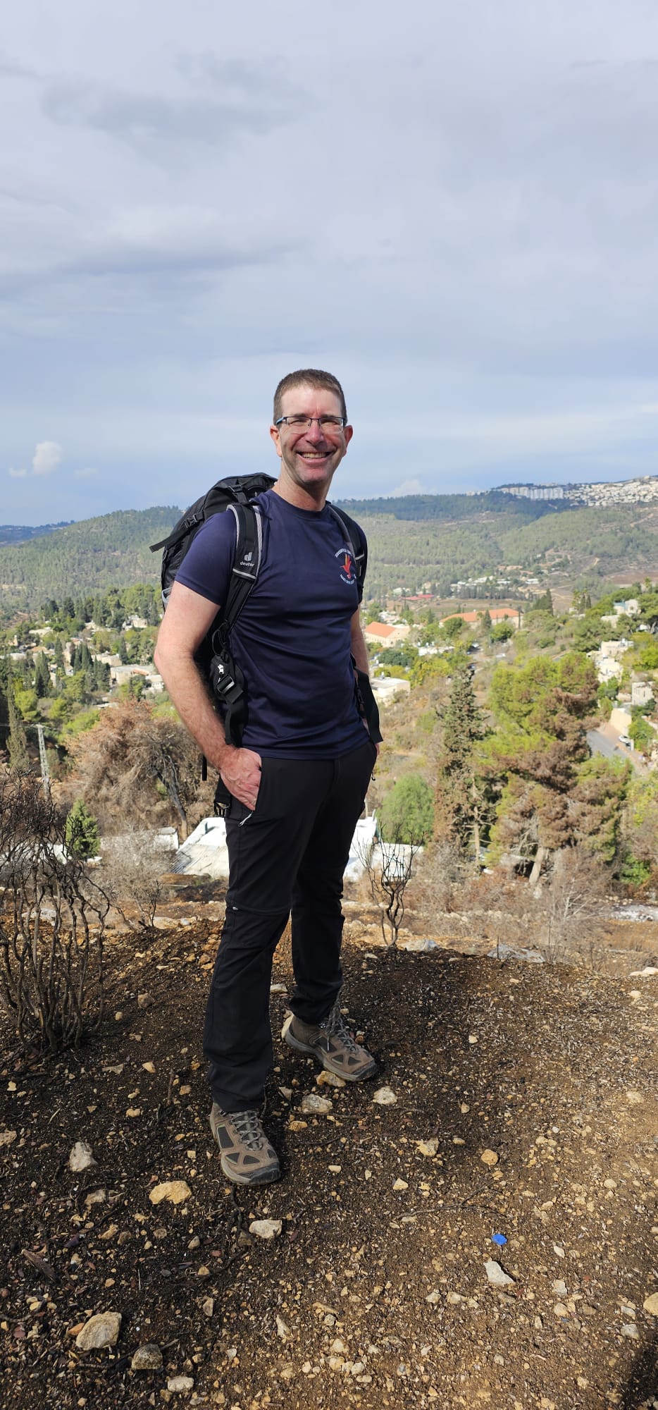 עידן מלין, מדריך הטיולים, עומד עם תרמיל גב מול נוף הגבעות