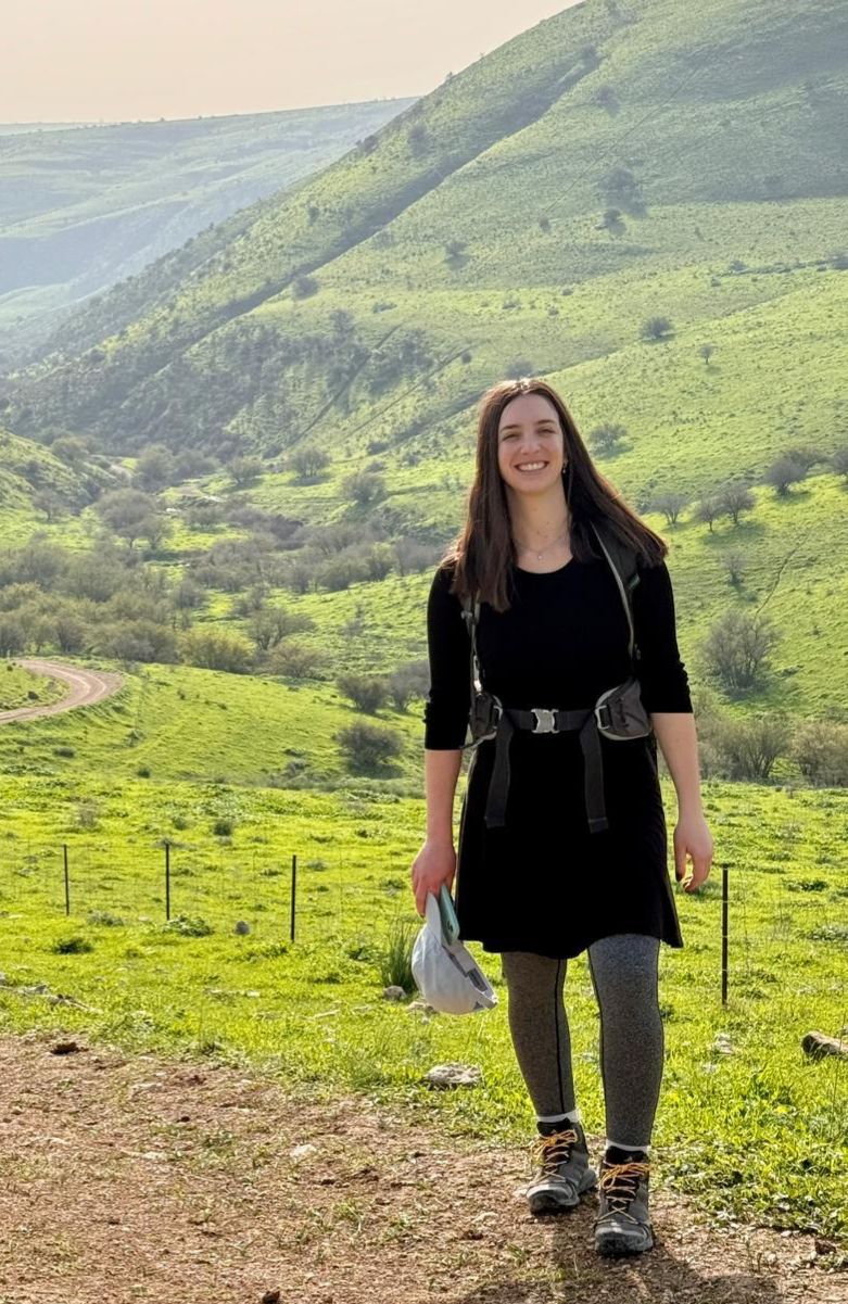 טל מלין, מדריכת הטיולים, עומדת עם תרמיל גב בשביל בין הגבעות הירוקות